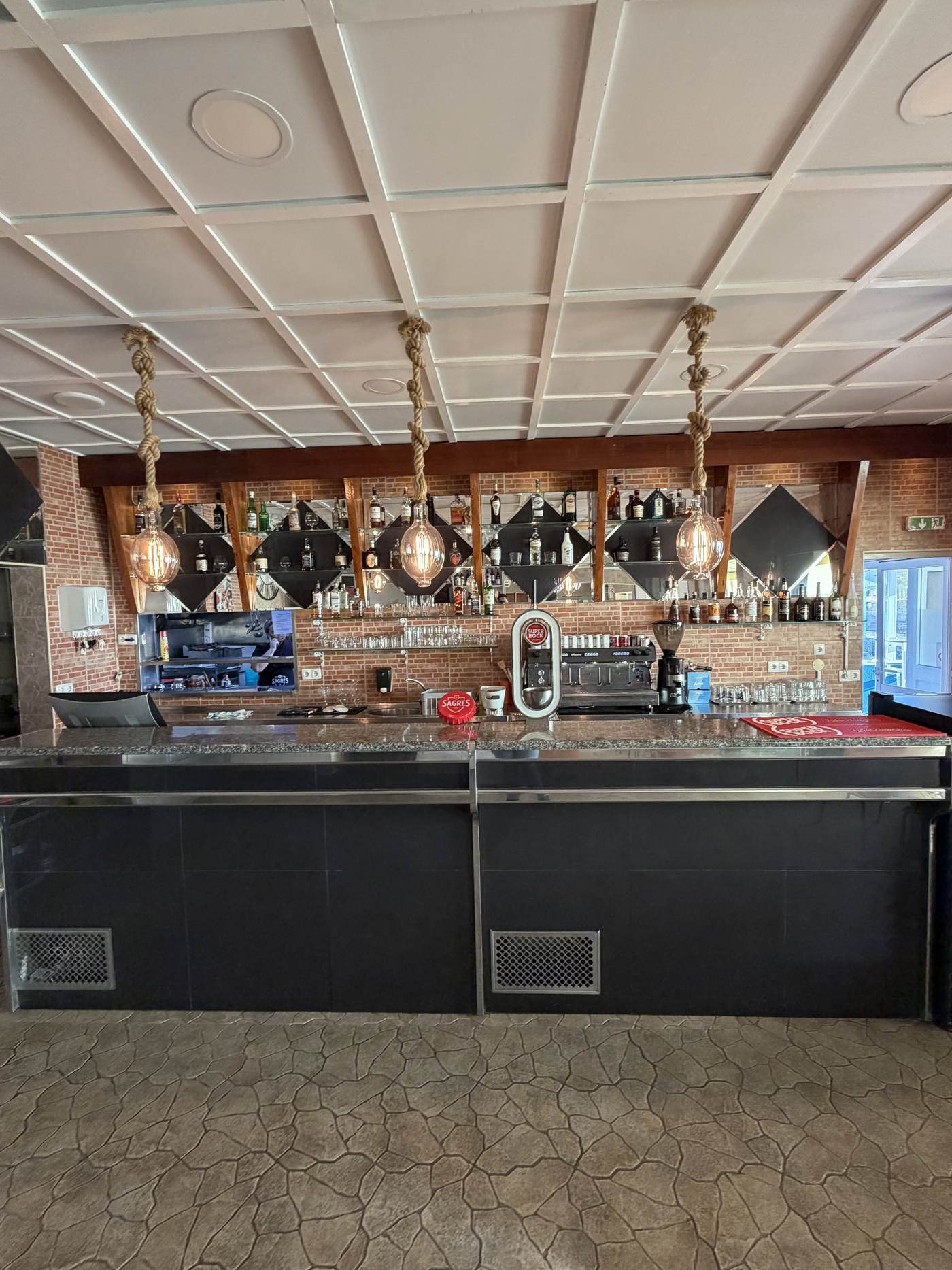 Balcão do restaurante em parede de tijolo, com a máquina de café e a garrafeira